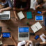 group of people sitting around a table with laptops and tablets